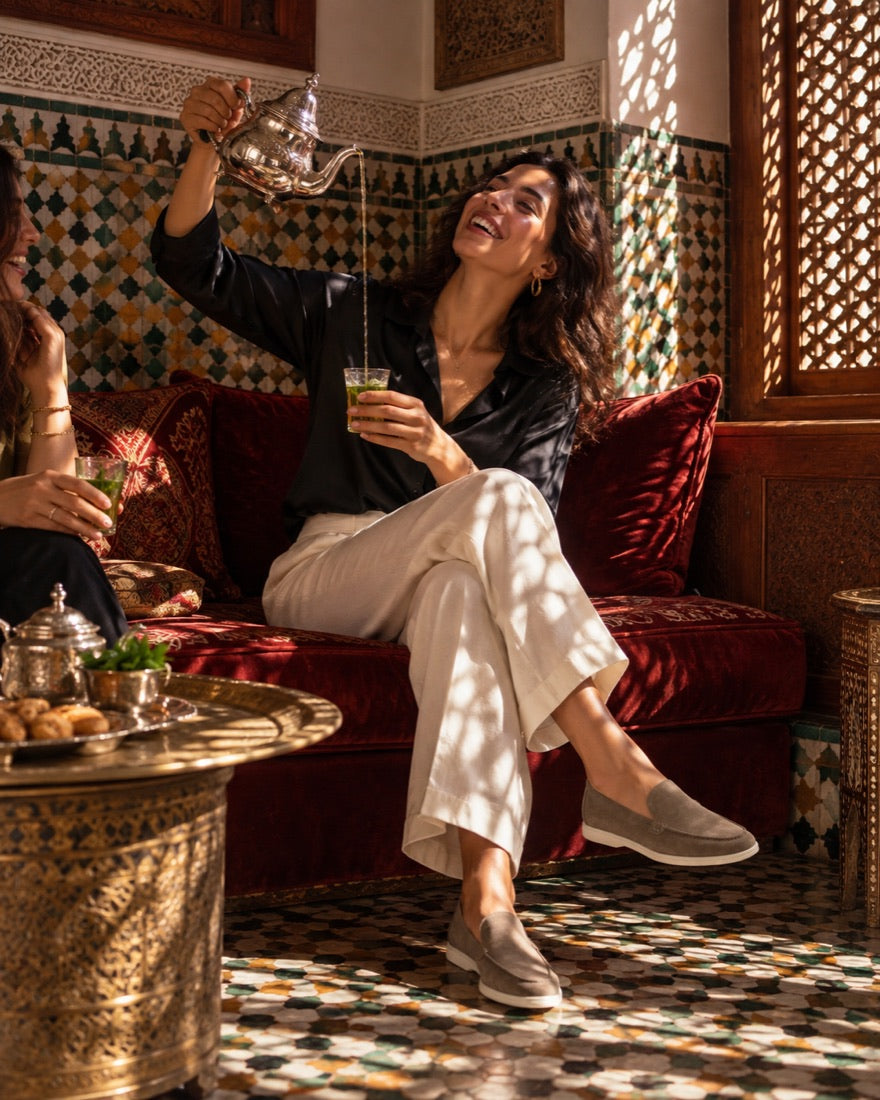 Une femme rit en servant le thé dans un riad de Fès, mocassins IZEM taupe